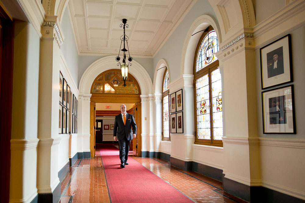 the man is walking down a hallway that has red carpet and a large chandelier