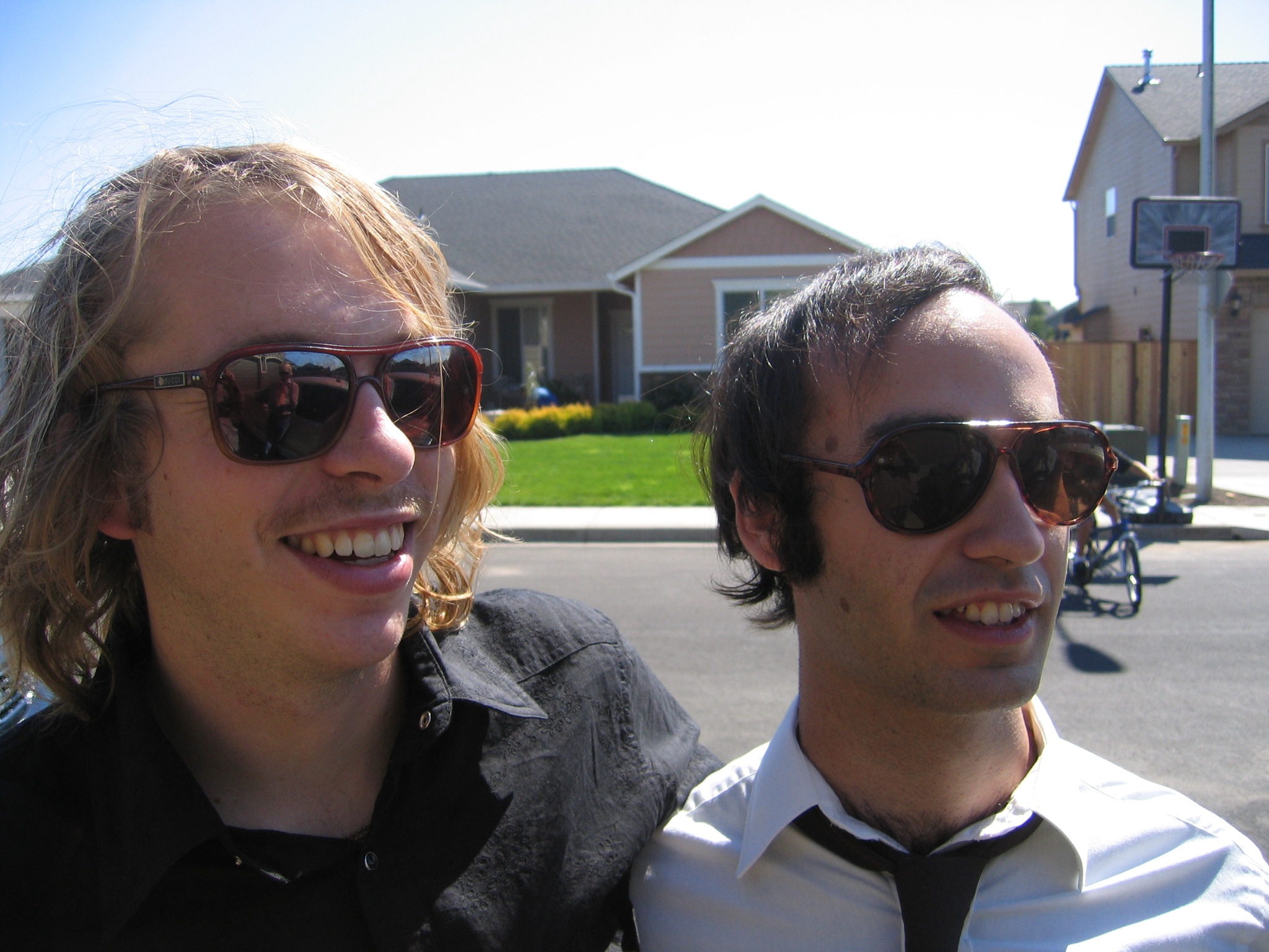 a man with long hair and sunglasses standing next to another man