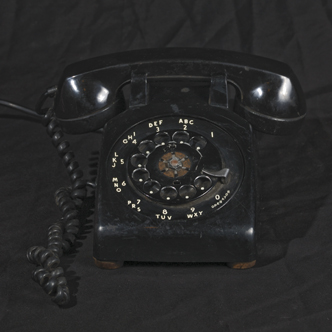 a black rotary phone sitting on a black sheet
