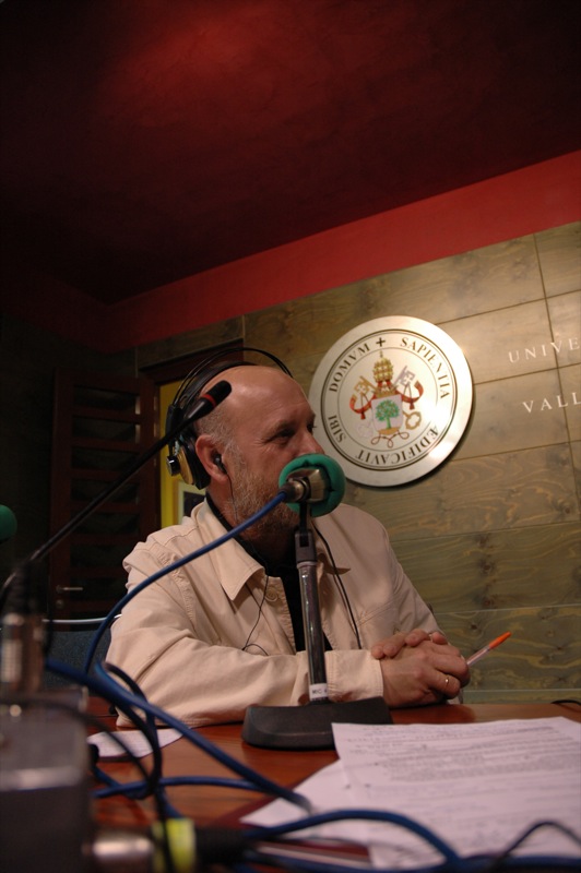 a man sits at a desk with a microphone and some papers