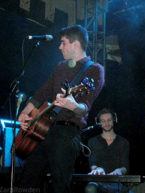 a young man playing guitar while standing in front of a microphone