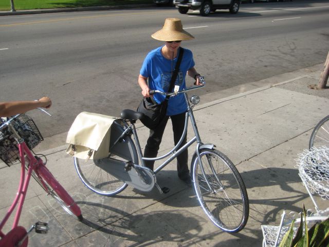 a woman wearing a hat with a basket riding a bike