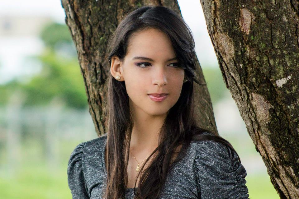 a girl poses against the tree in a gray shirt