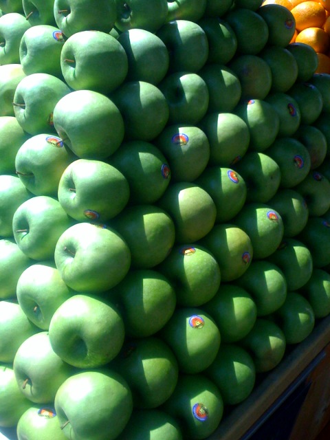 piles of green apples and oranges for sale at market