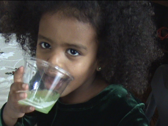 young black child drinking green smoothie from glass