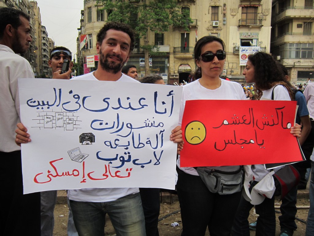 two protesters with protest signs in arabic and english