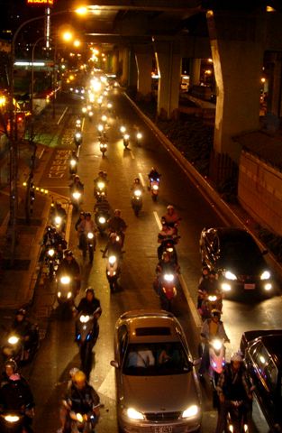 a bunch of motorcycles and cars moving down a street at night