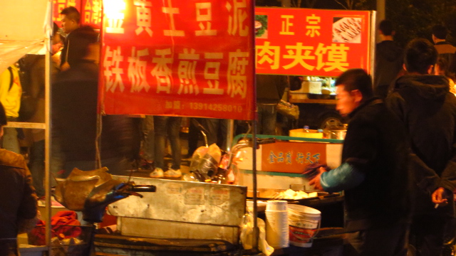 people standing around outside by street food stand