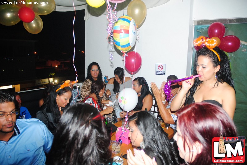 a party with people in front of balloons and a woman with a cigarette in her mouth