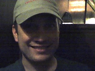 man smiling while in a restaurant, wearing a hat