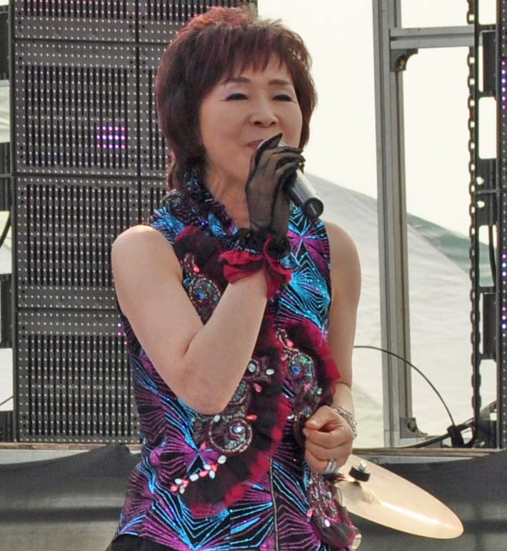 asian woman performing on stage with microphone in front of screen