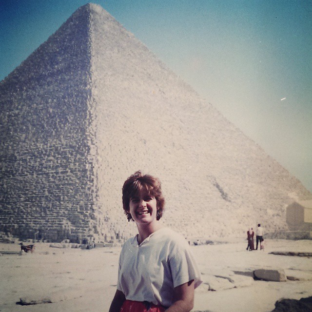 a woman standing in front of a giant pyramid with people nearby