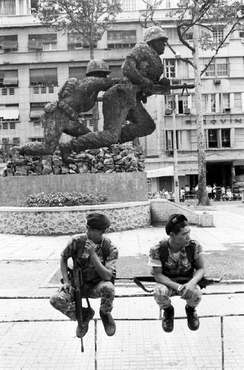 two soldiers sitting on a bench with a statue in the background