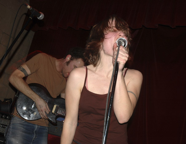 a girl singing into a microphone while someone plays guitar behind her