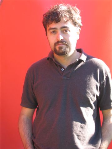 a bearded man stands next to a red background