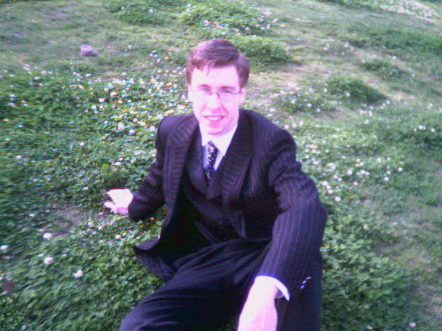 a young man in a suit and tie sitting down on the ground