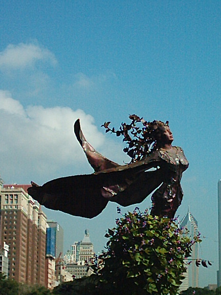 a statue stands in front of tall buildings