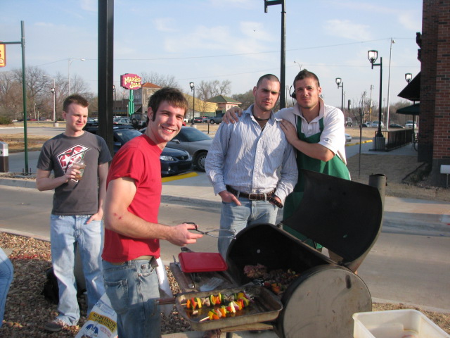 four guys are posing with a barbecue grill outside