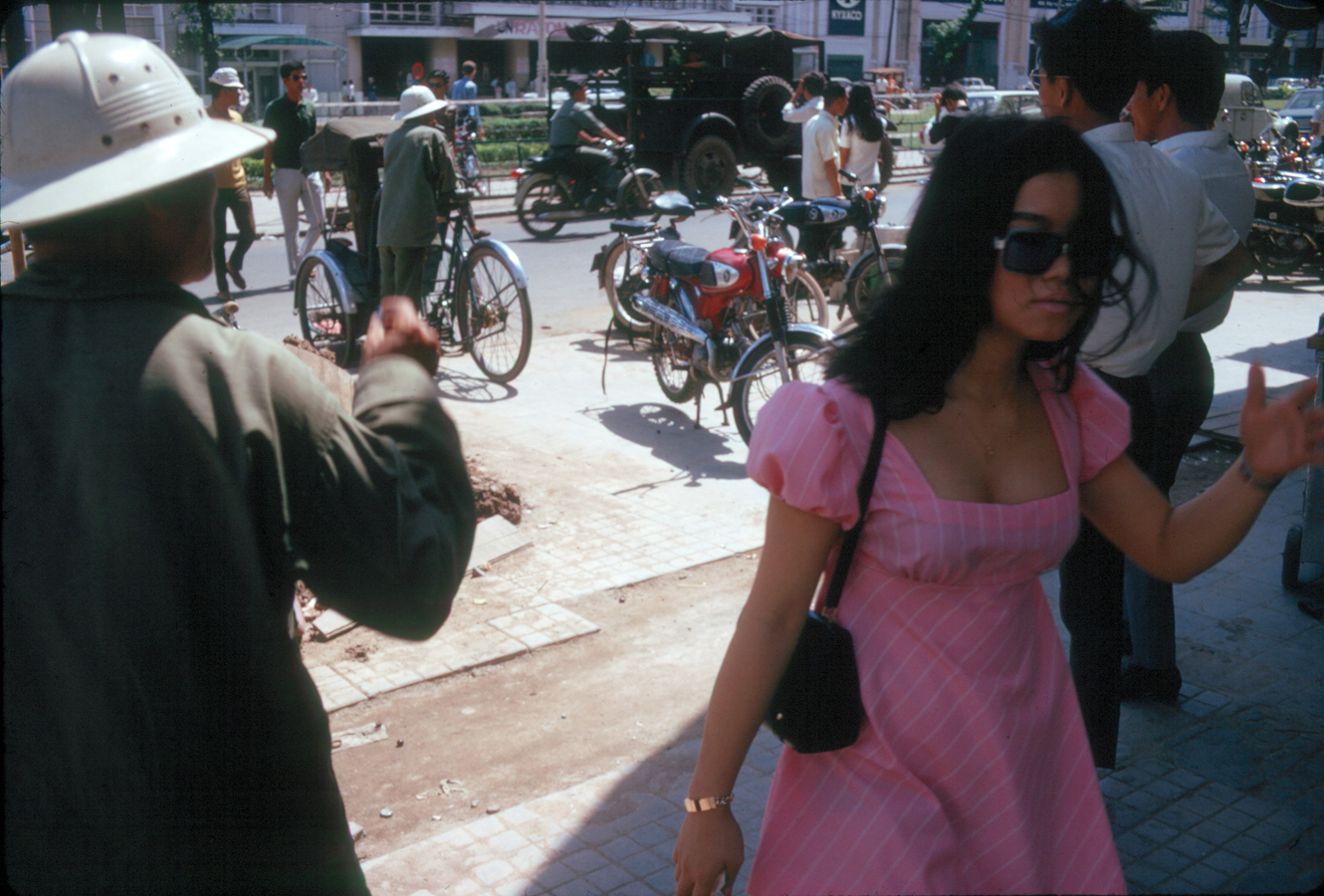 a woman in a pink dress walking near men on bicycles