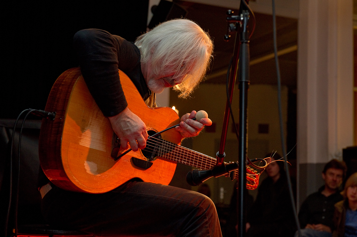 an old man playing a guitar in front of a crowd