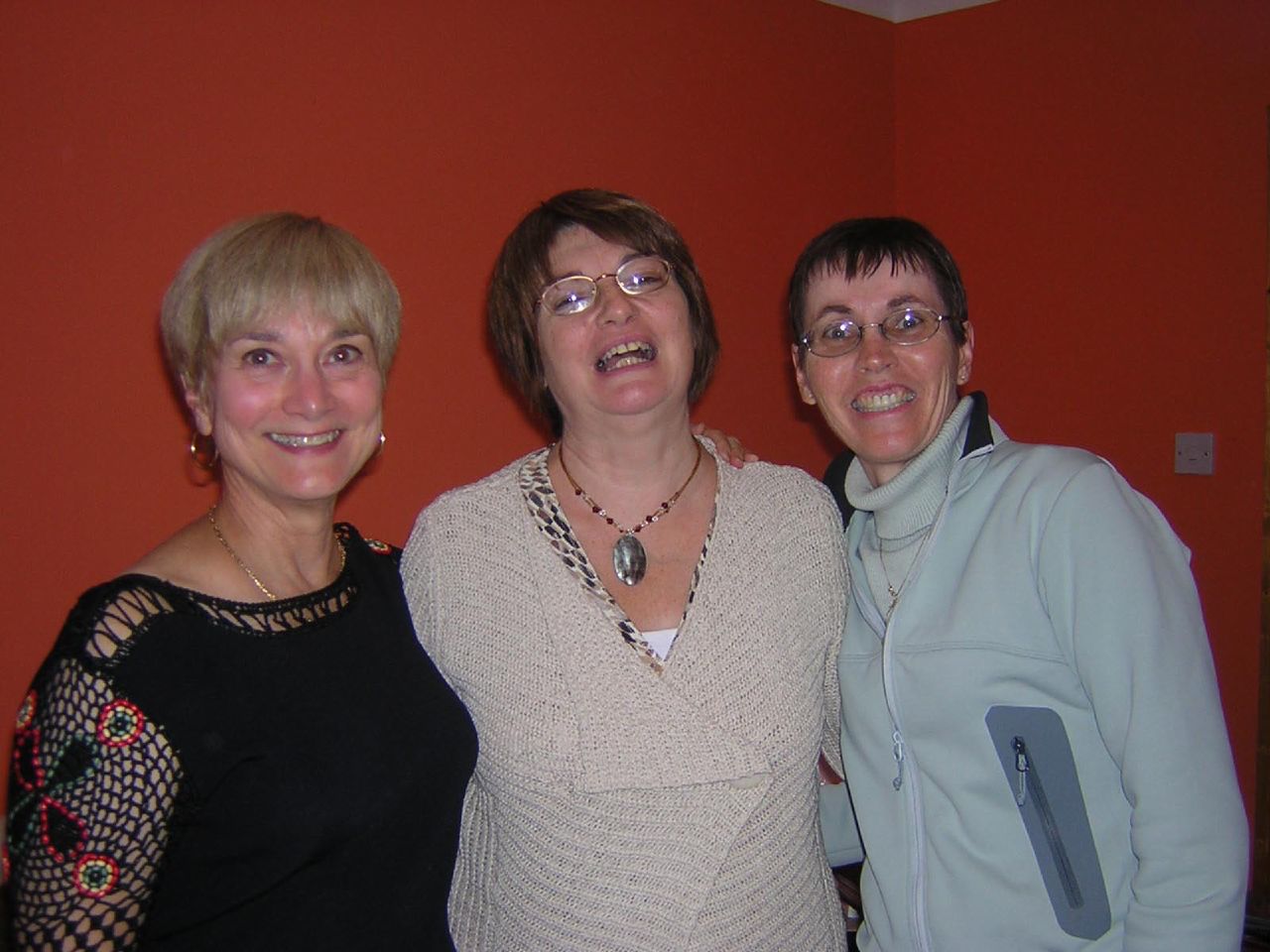 three women smiling for the camera with an orange background