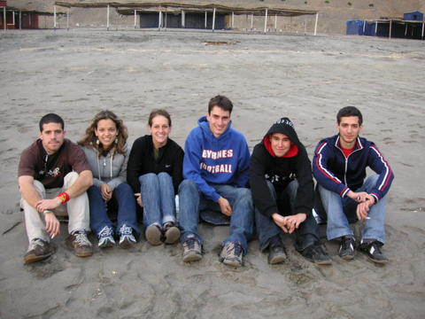 six people in black and blue sweatshirts sitting on a beach