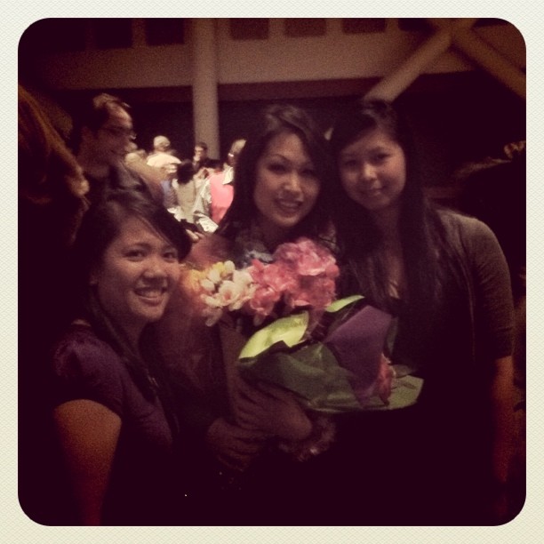 three young ladies are holding colorful flowers and smiling