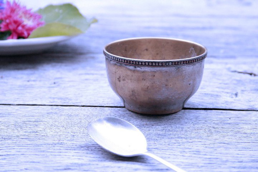 an old metal bowl and spoon are sitting on the table