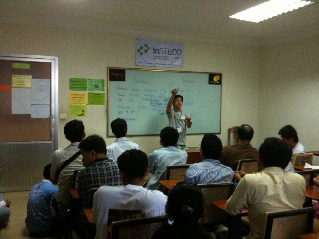 group of students sitting in classroom with one person standing up speaking to them