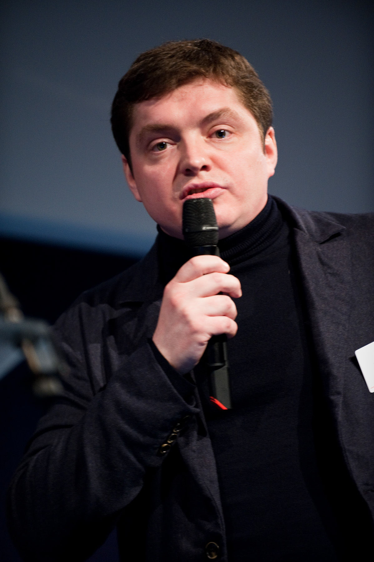 a man is talking into the microphone wearing a black jacket