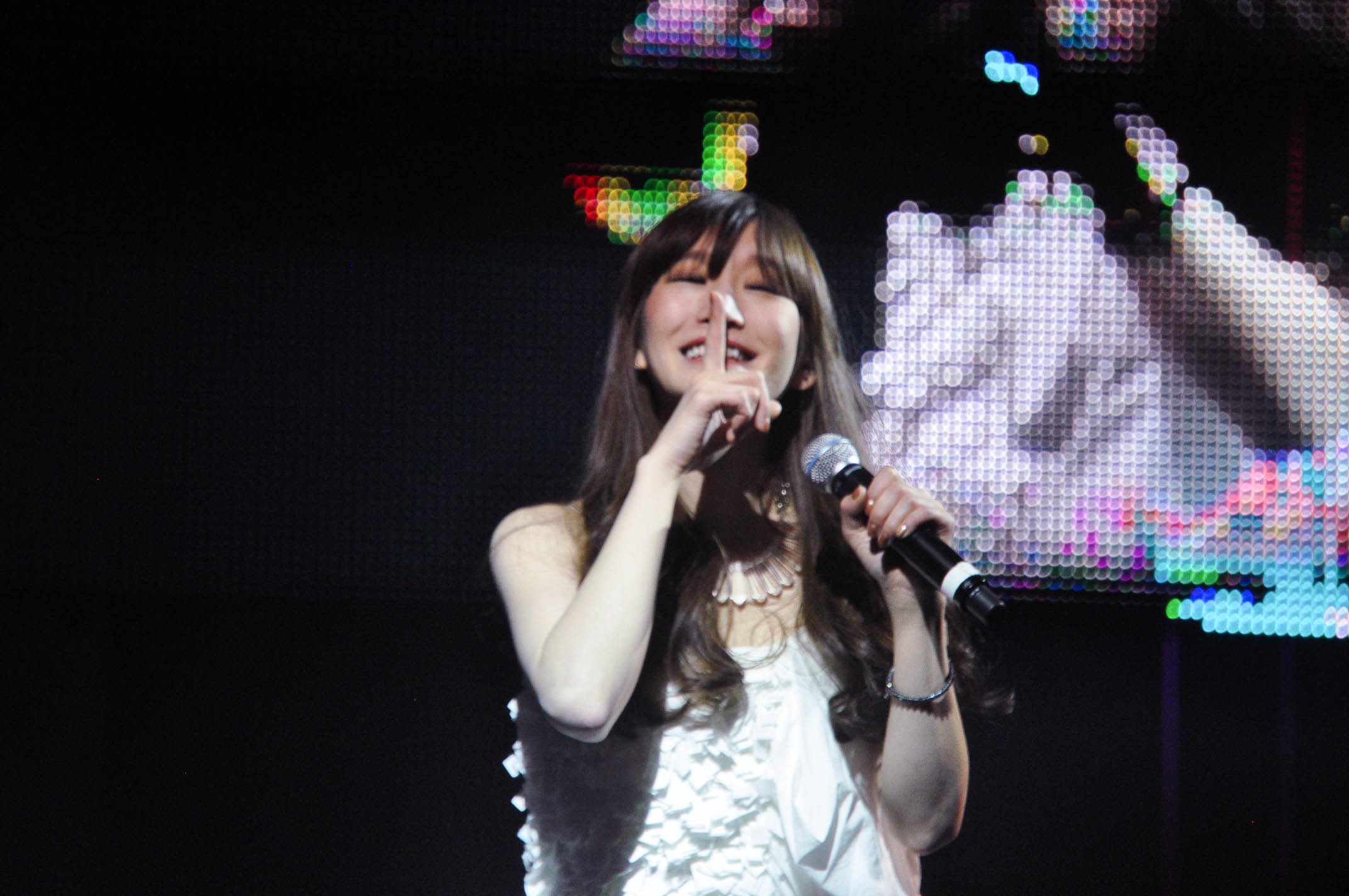 woman standing on stage with microphone looking up at the camera