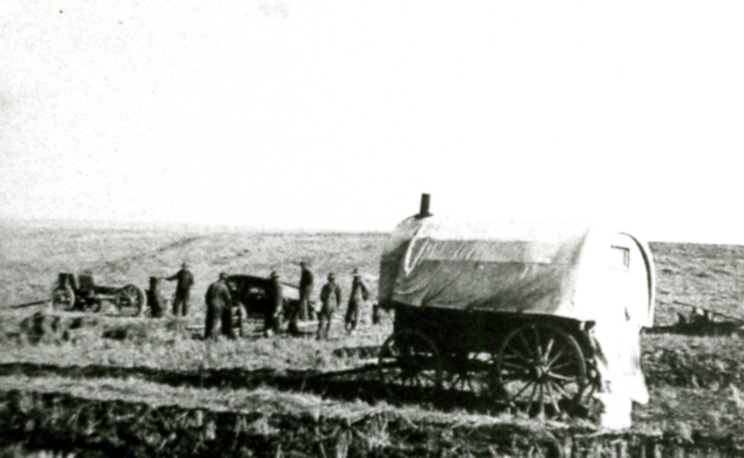 an old pograph of a person in front of a covered wagon