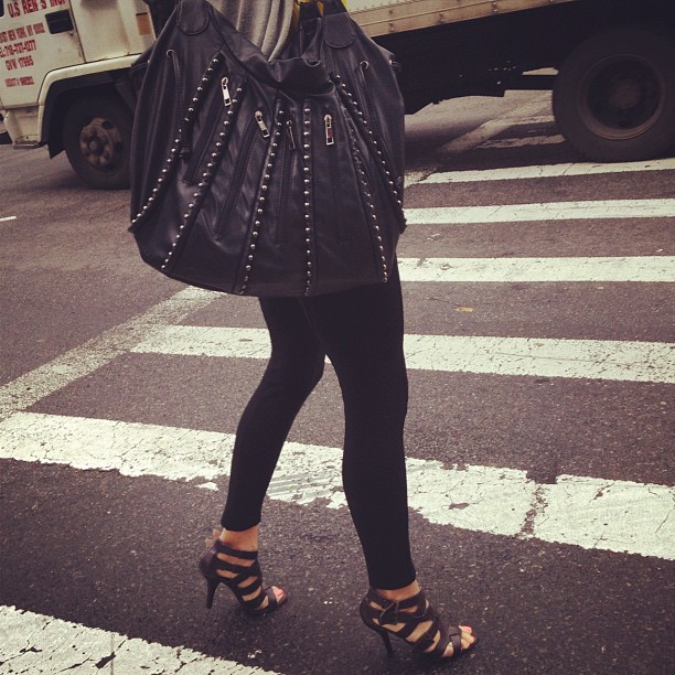 a woman is carrying a black handbag down the street
