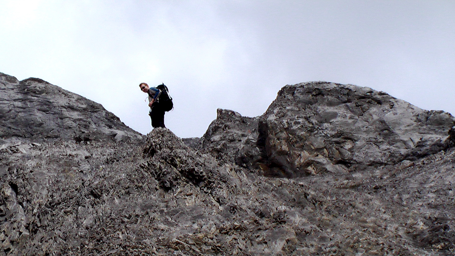 a man with a backpack and backpack stands on top of a large rock