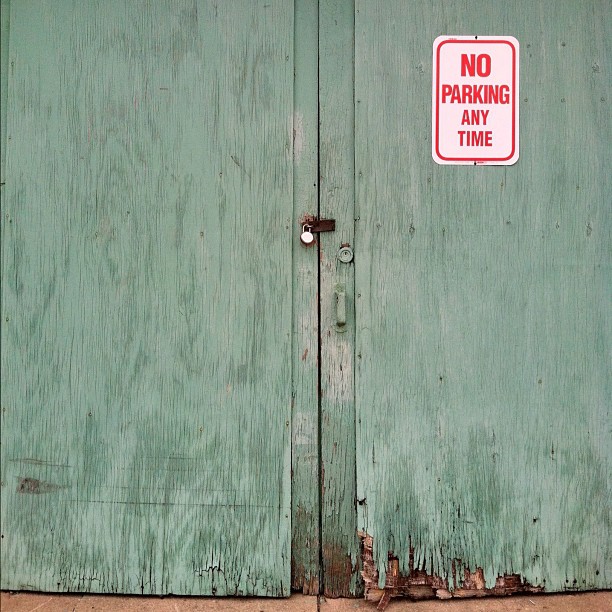 a green wooden door with a no parking sign on it