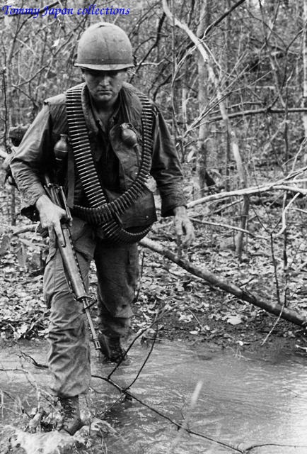 black and white pograph of man in waders crossing stream