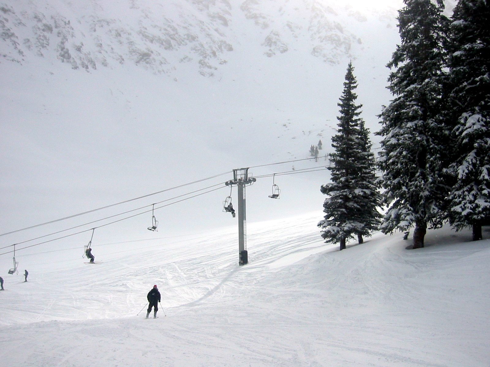 people snow skiing down a mountain with lift cars