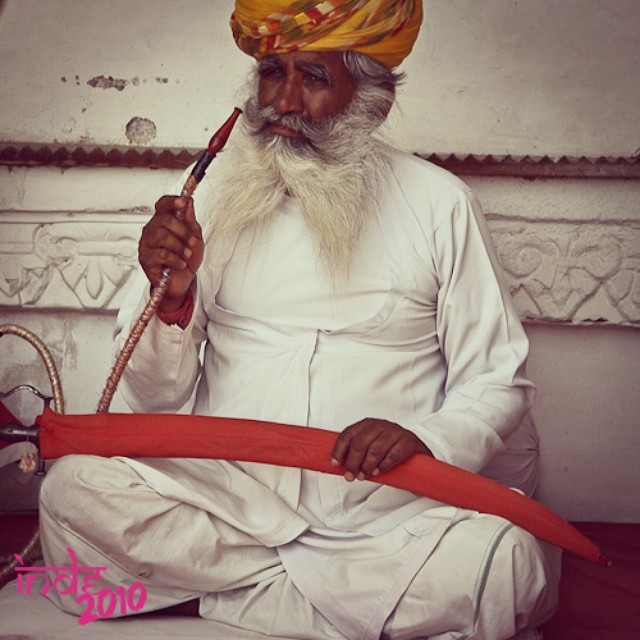 an old indian man smoking a pipe next to a pipe holder