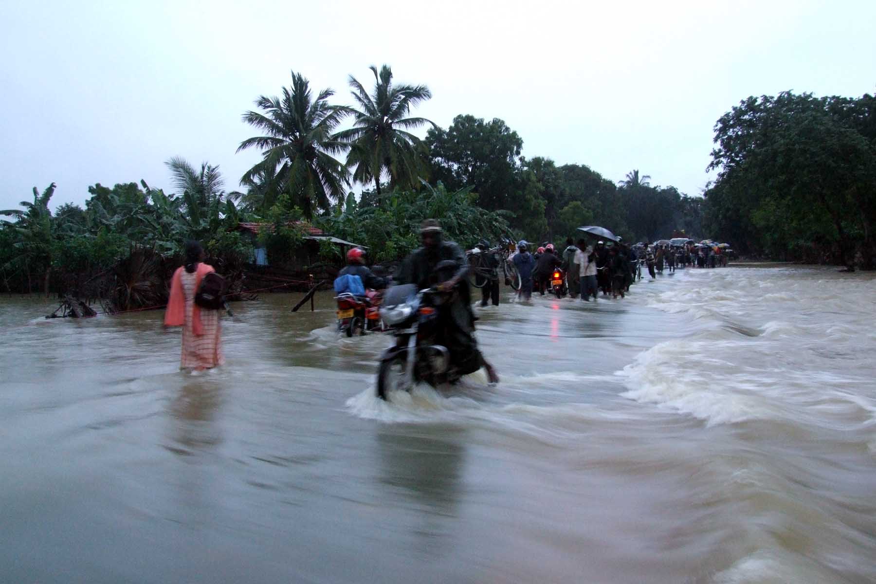 a line of people riding motorcycles across a flooded street