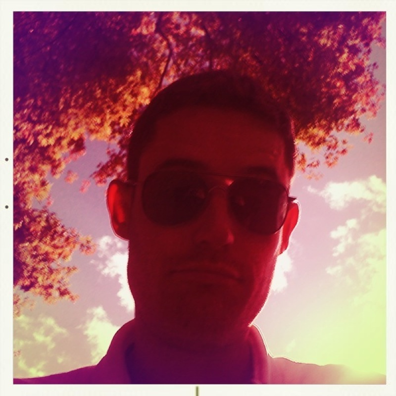 man wearing sunglasses standing under large tree in front of sun