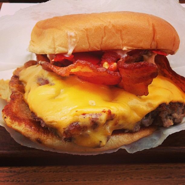 a cheeseburger with bacon and tomatoes in a bun on top of wood