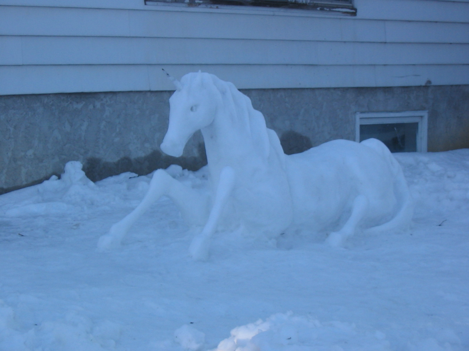 a snow horse standing in the snow by the side of a building