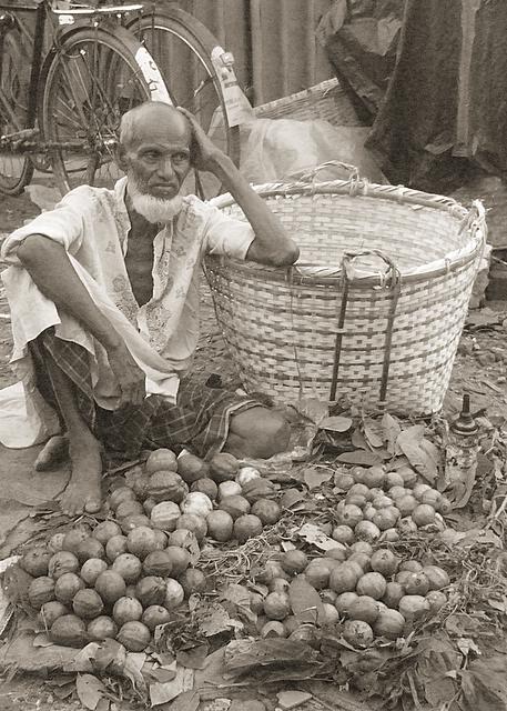 old man squatted in front of an assortment of fruit