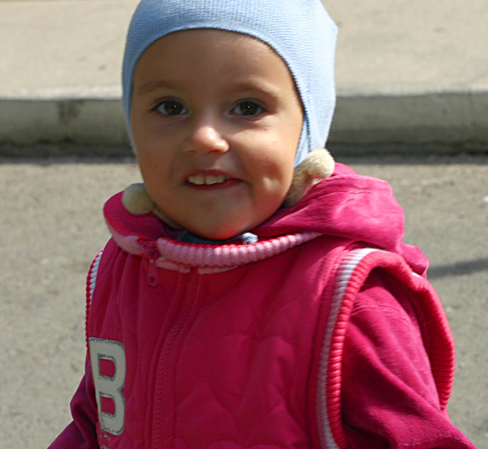 a smiling baby girl wearing a blue knit hat and pink coat
