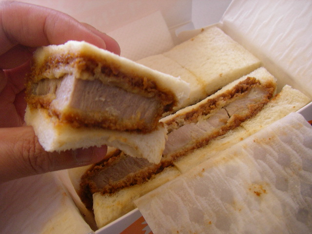 a hand holding a pastry filled with meat inside of a box