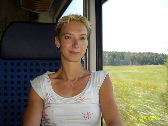 a woman smiling and riding a train by some trees