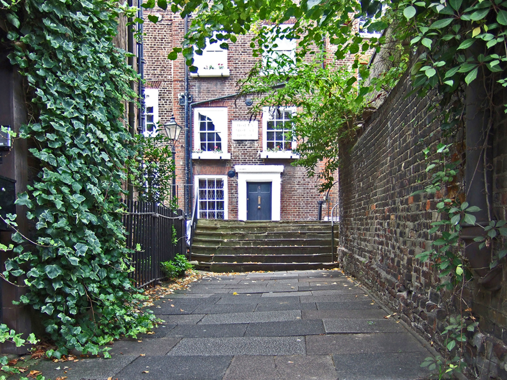 a street that has ivy on the wall and stairs leading up to the houses