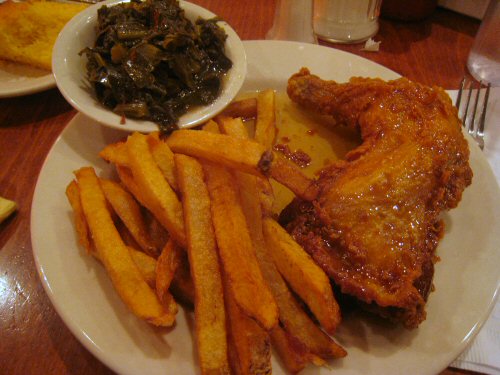 a plate with french fries, meat and a bowl of greens