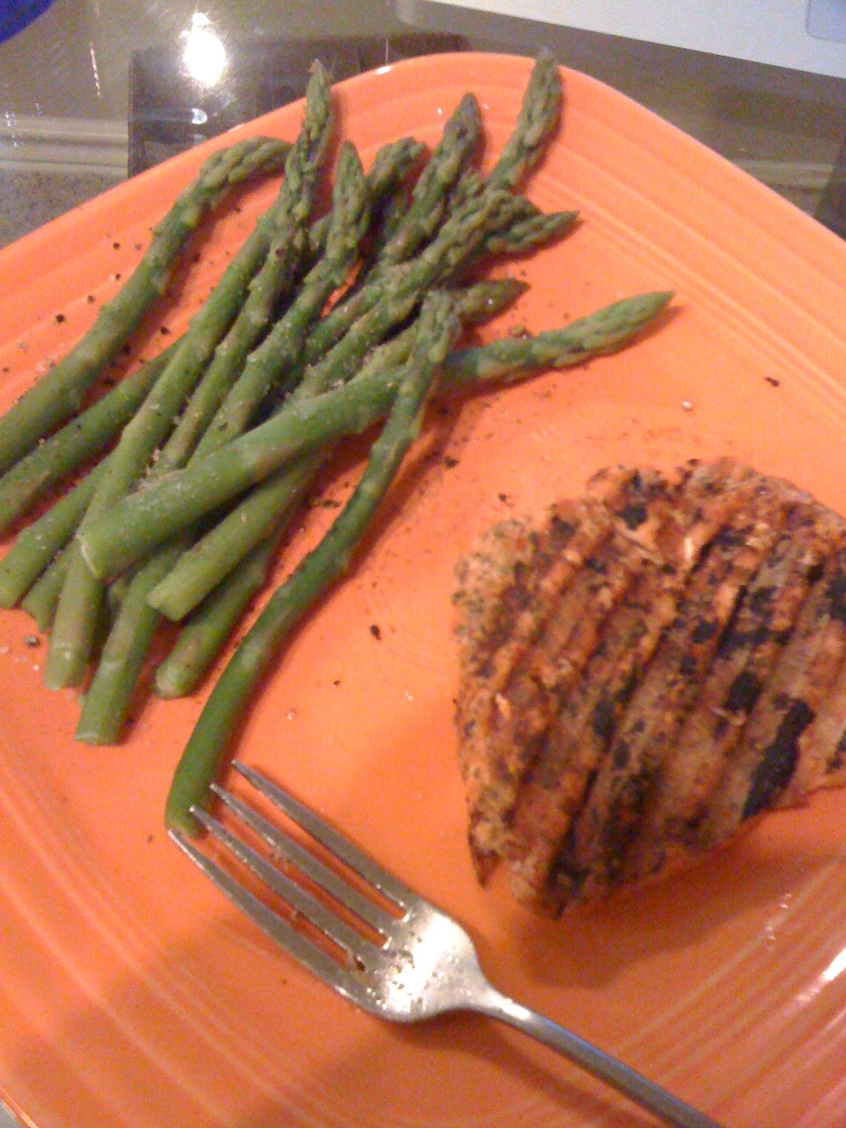 meat and asparagus on an orange plate with a fork