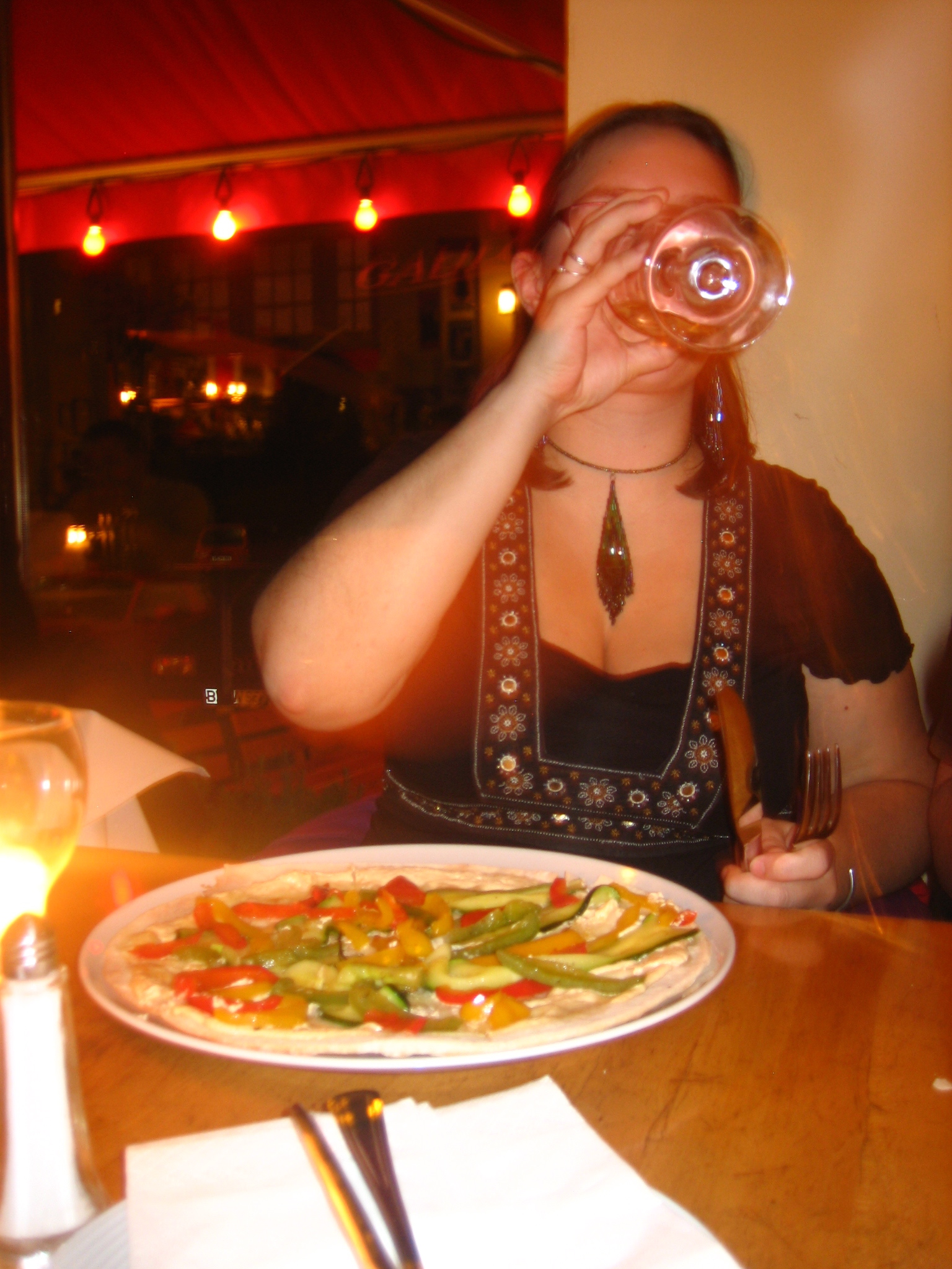 a woman drinking from a bottle while sitting in front of a pizza